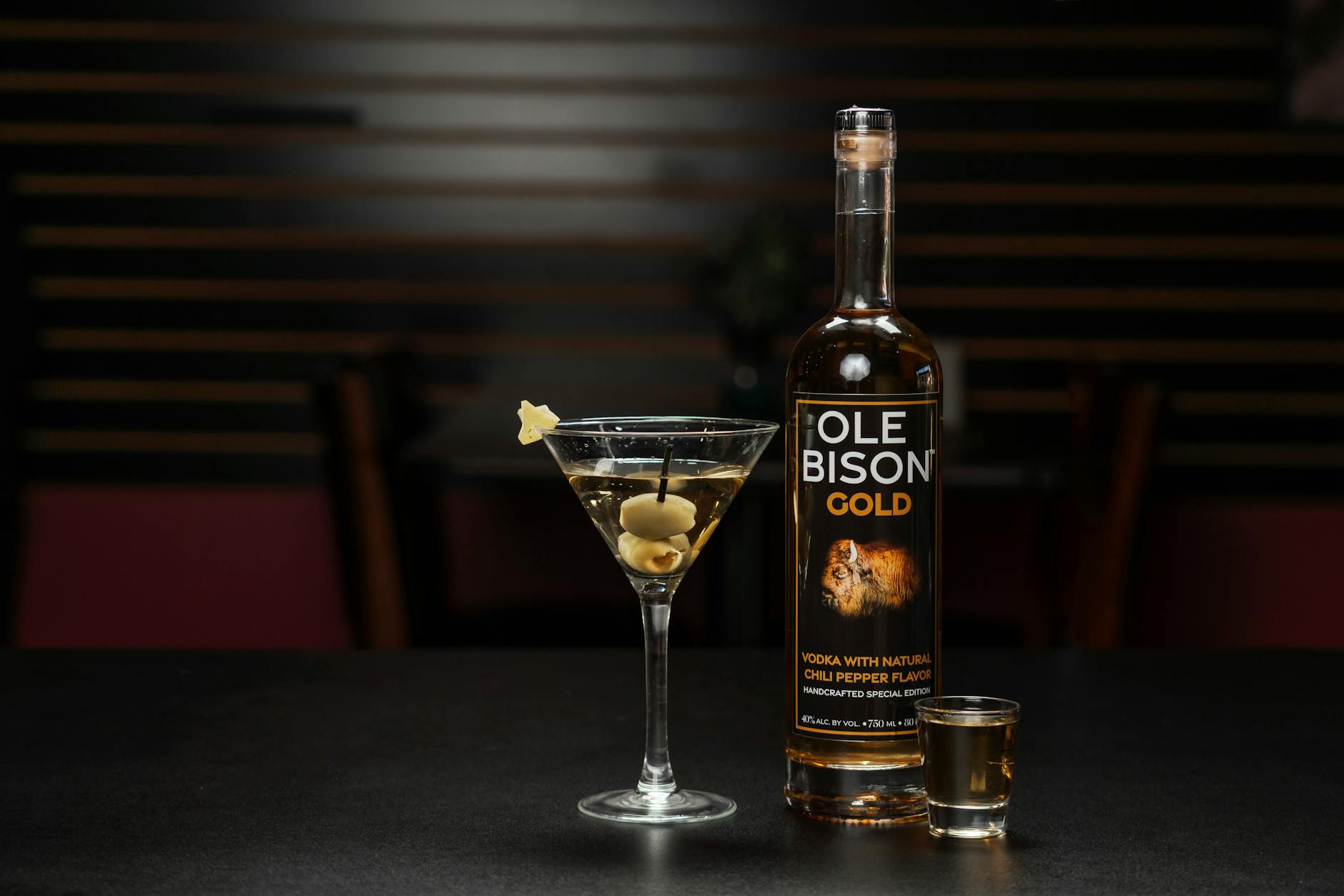 Sophisticated bar presentation with Ole Bison Gold Vodka, martini glass, and shot glass on a dark countertop.