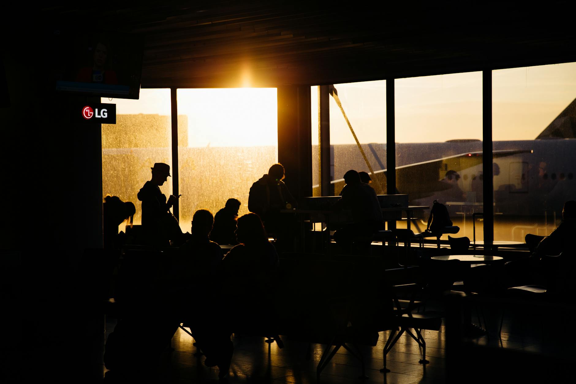Travelers sitting in an airport terminal at sunset, silhouetted against the backdrop of an airplane.